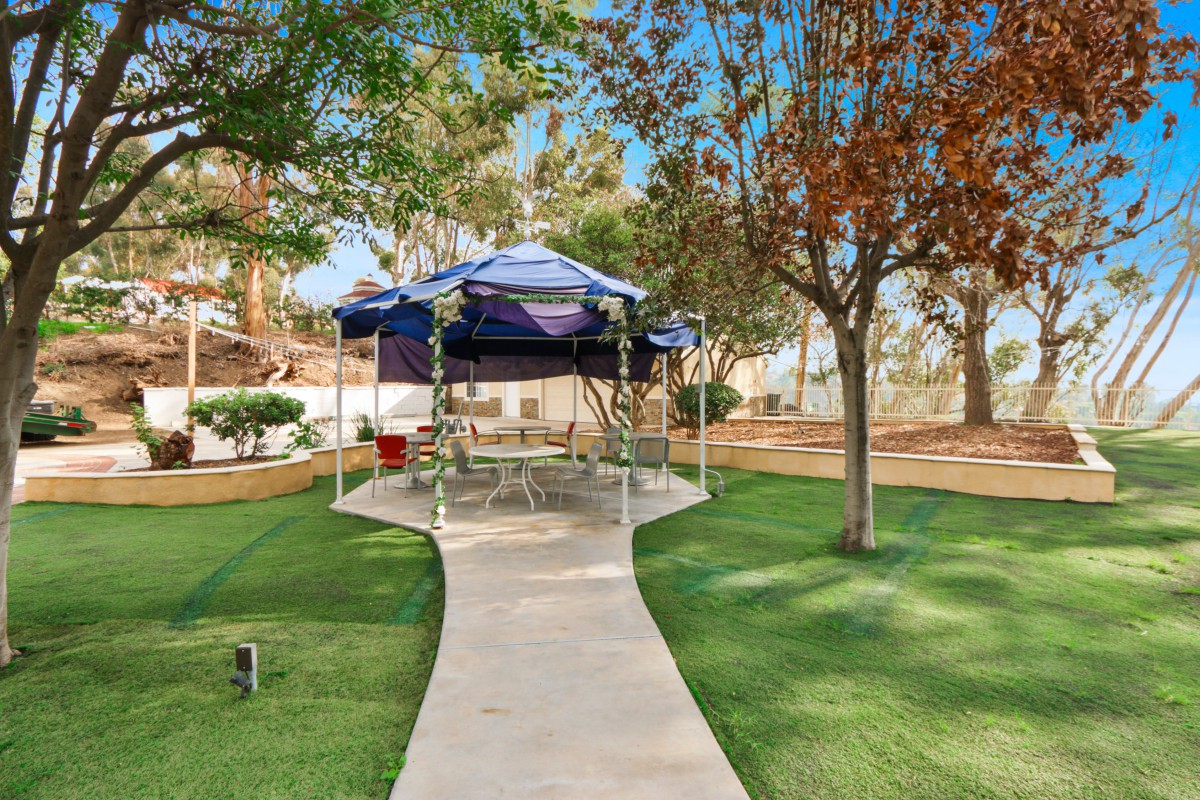 A gazebo in a park surrounded by trees and a well-maintained lawn.