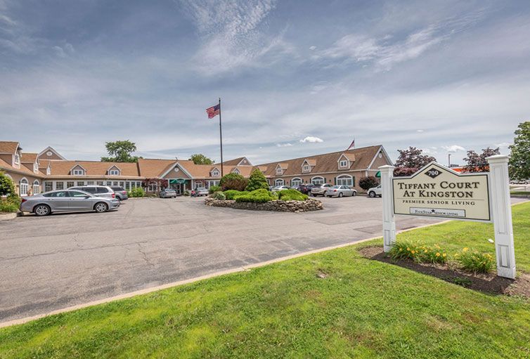 A hotel with a parking lot and an American flag, featuring a welcoming sign.