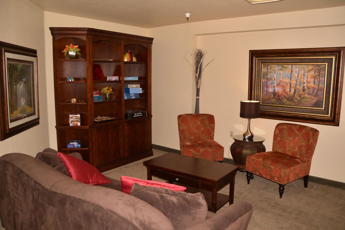 A cozy living room with a bookshelf, chairs, sofa, and table.