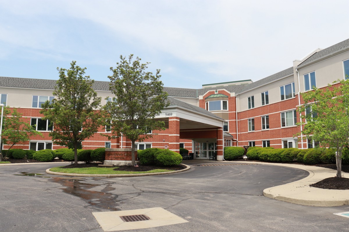 A view of a hotel exterior with a driveway and surrounding trees.