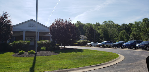 A serene outdoor view featuring a tree, well-manicured grass, and a nearby parking area.