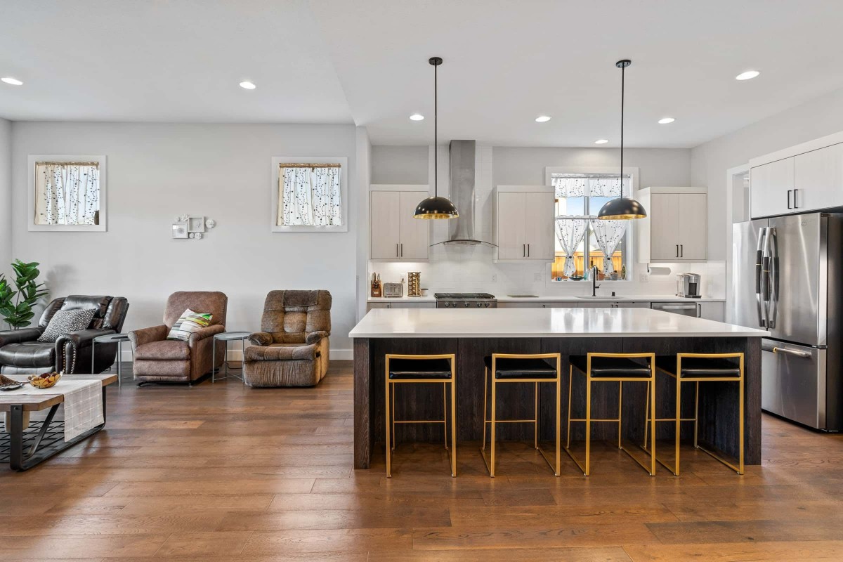 A modern kitchen with an island and bar stools, featuring pendant lighting and hardwood flooring.