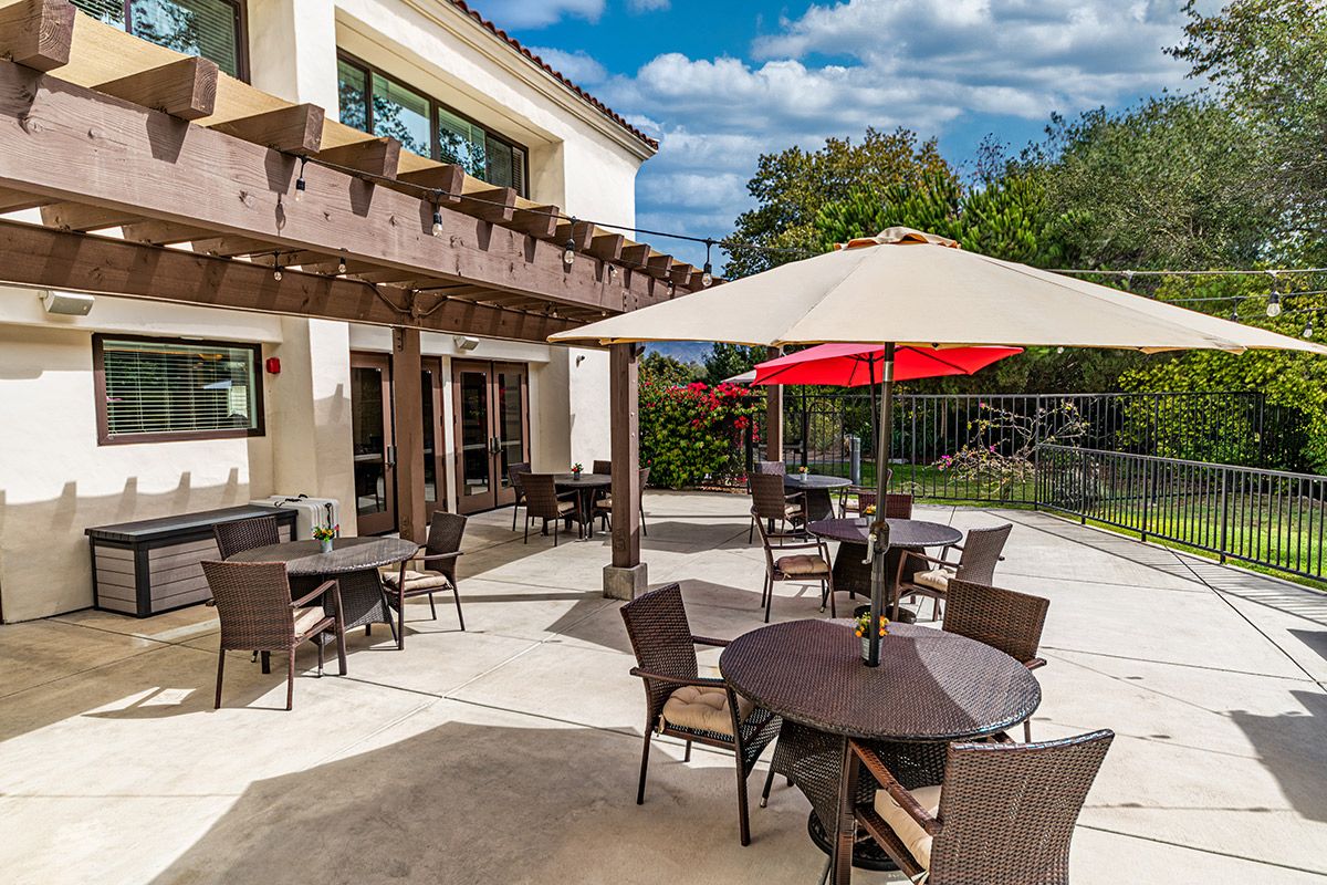 A sunny outdoor patio area with tables and chairs under umbrellas.
