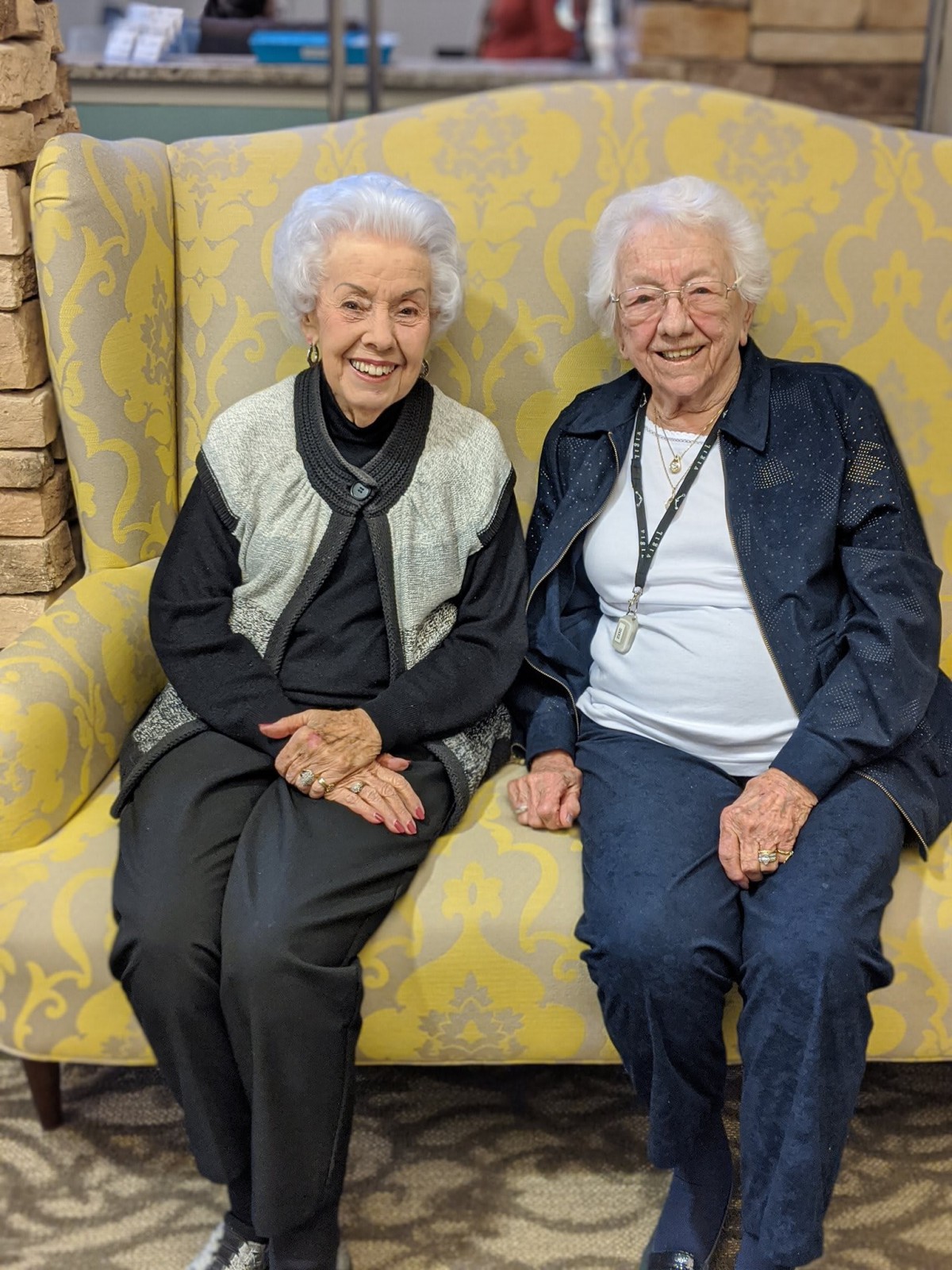Two elderly women sitting together on a couch, smiling.