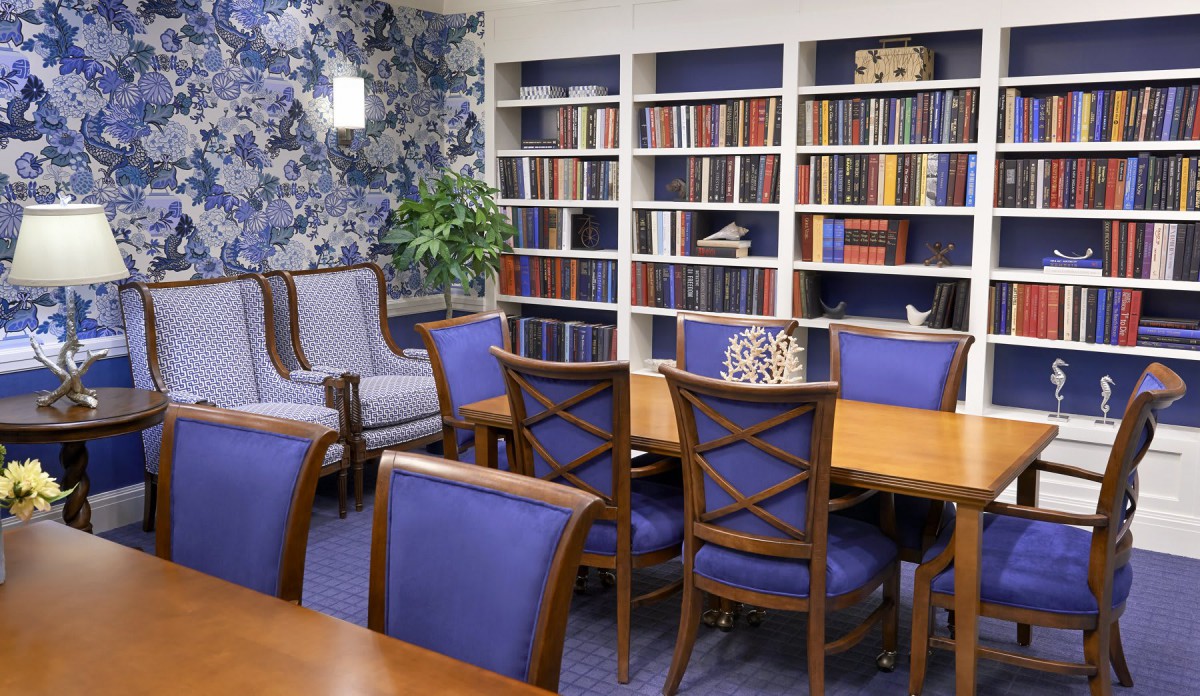 A cozy library room with bookshelves, a large table, and comfortable chairs.