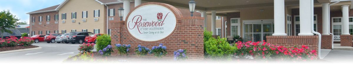 A brick wall with a sign for 'The Rosewood,' featuring flowers and a lamp post.