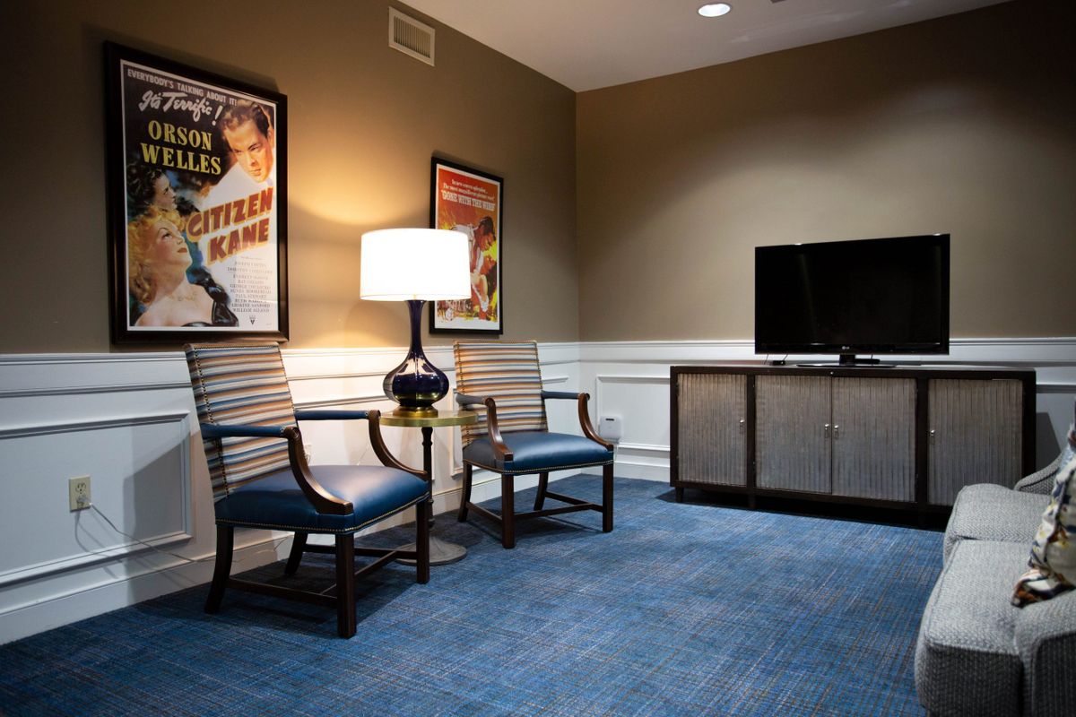 A cozy living room with two chairs, a lamp, and a television, adorned with movie posters on the walls.