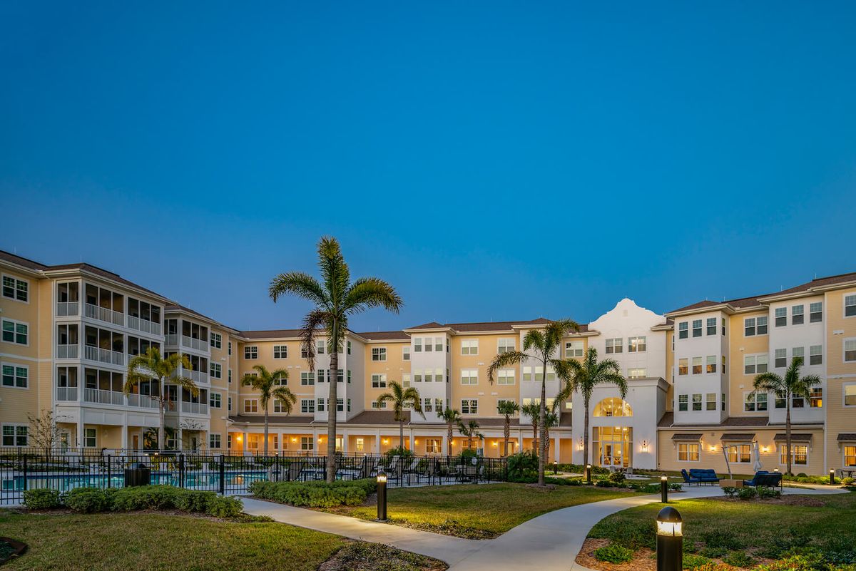 A well-lit residential building with palm trees in the evening.