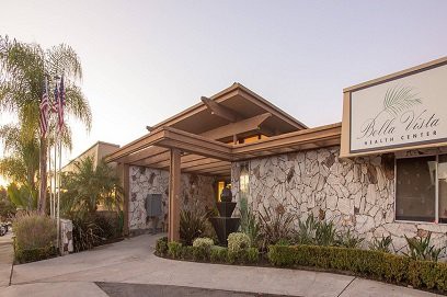 A stone-walled building with a wooden entrance surrounded by landscaping.
