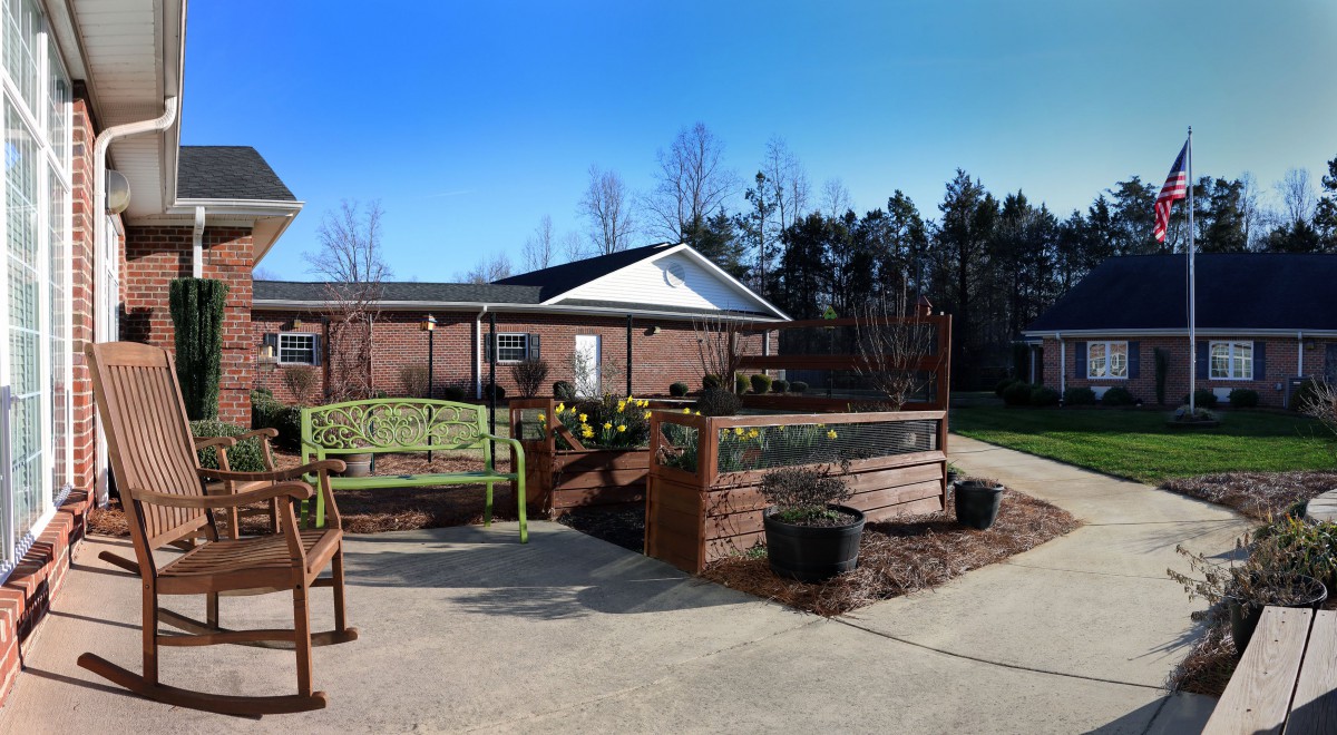 An outdoor area with benches and a garden in front of a brick building under a clear blue sky.