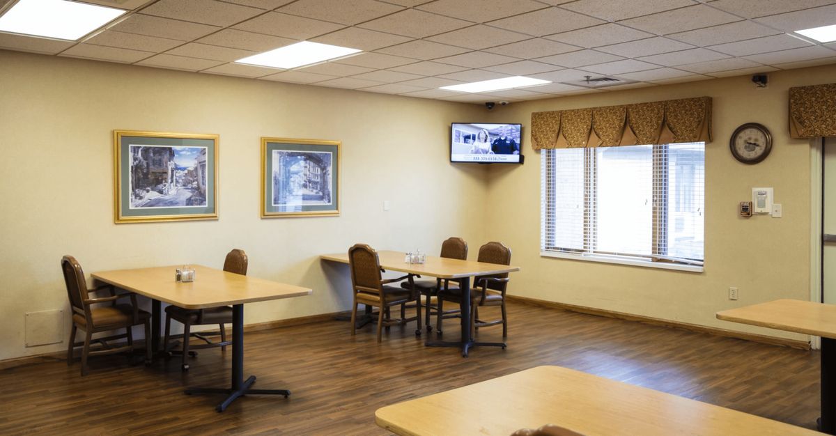 A small cafeteria with tables and chairs, a TV on the wall, and artwork hanging on the walls.