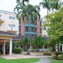 A multi-story building surrounded by palm trees and landscaped gardens.