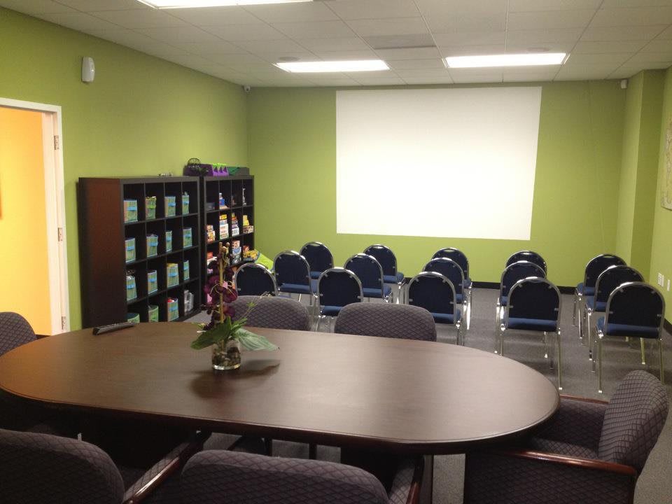 A meeting room with a projector screen, chairs arranged in rows, and bookshelves along the wall.