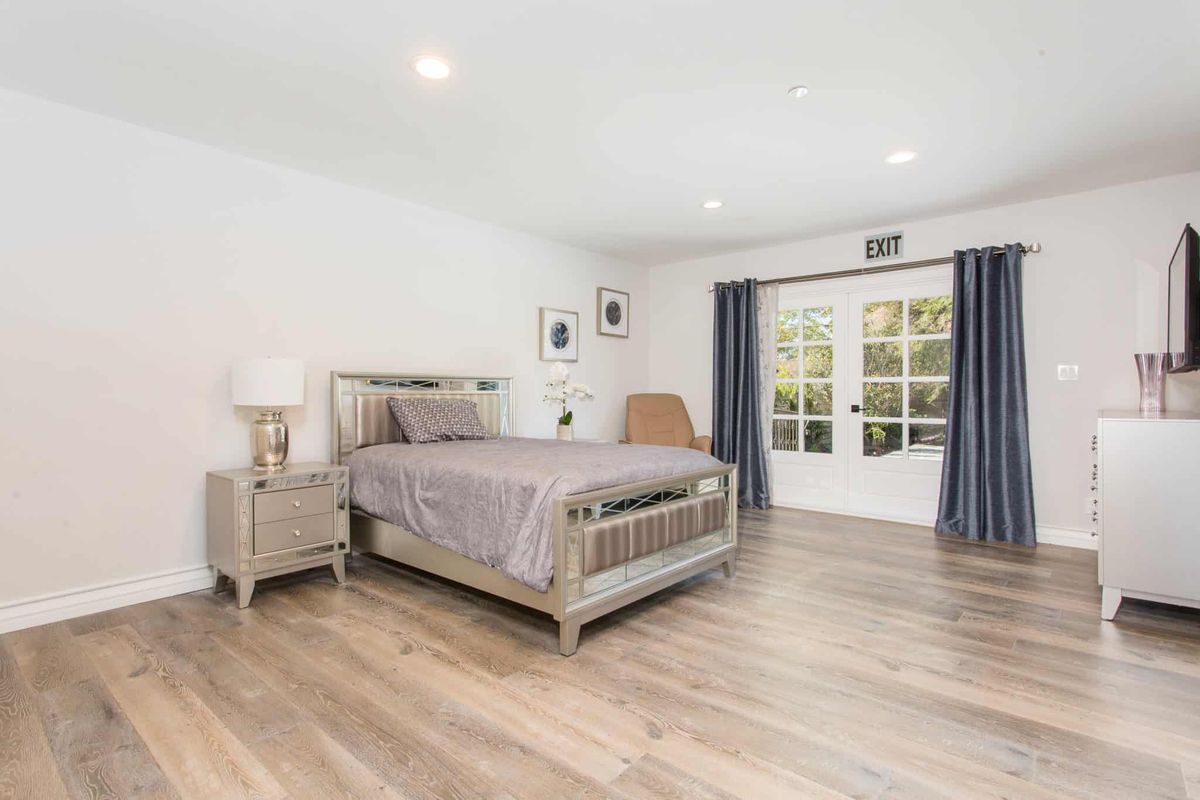 A modern bedroom featuring a wooden bed, nightstand, and floor, complemented by dark curtains and a glass door.