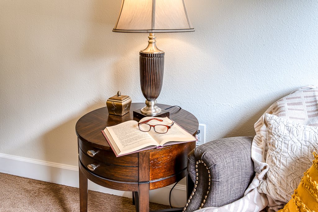 A cozy bedroom scene with a lamp, book, and glasses on a side table.