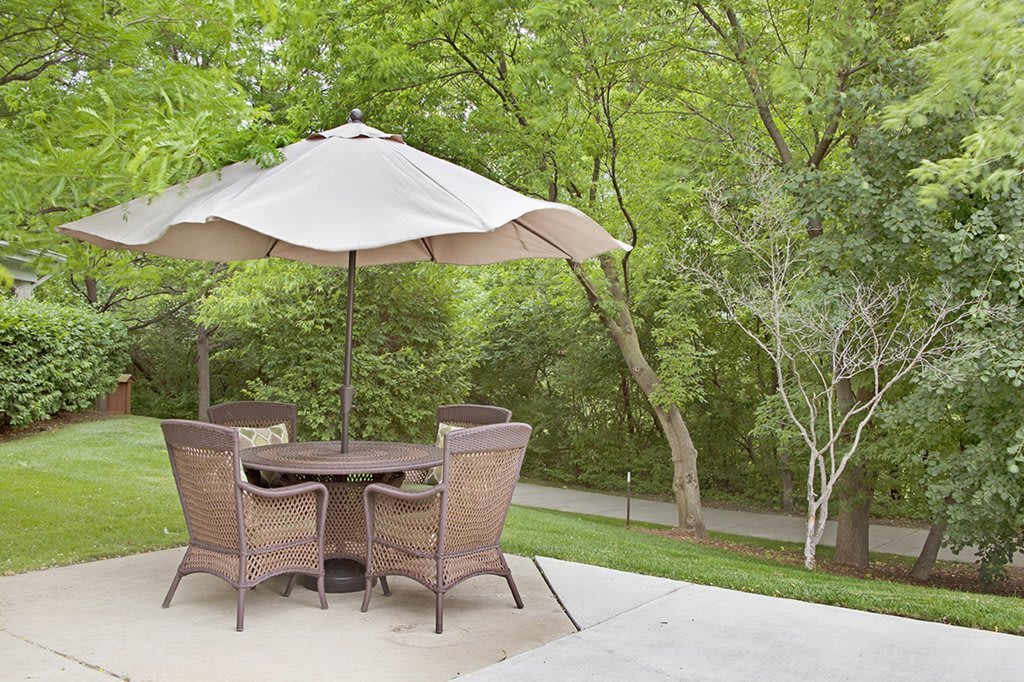 A peaceful patio setup with a table, chairs, and an umbrella surrounded by lush greenery.