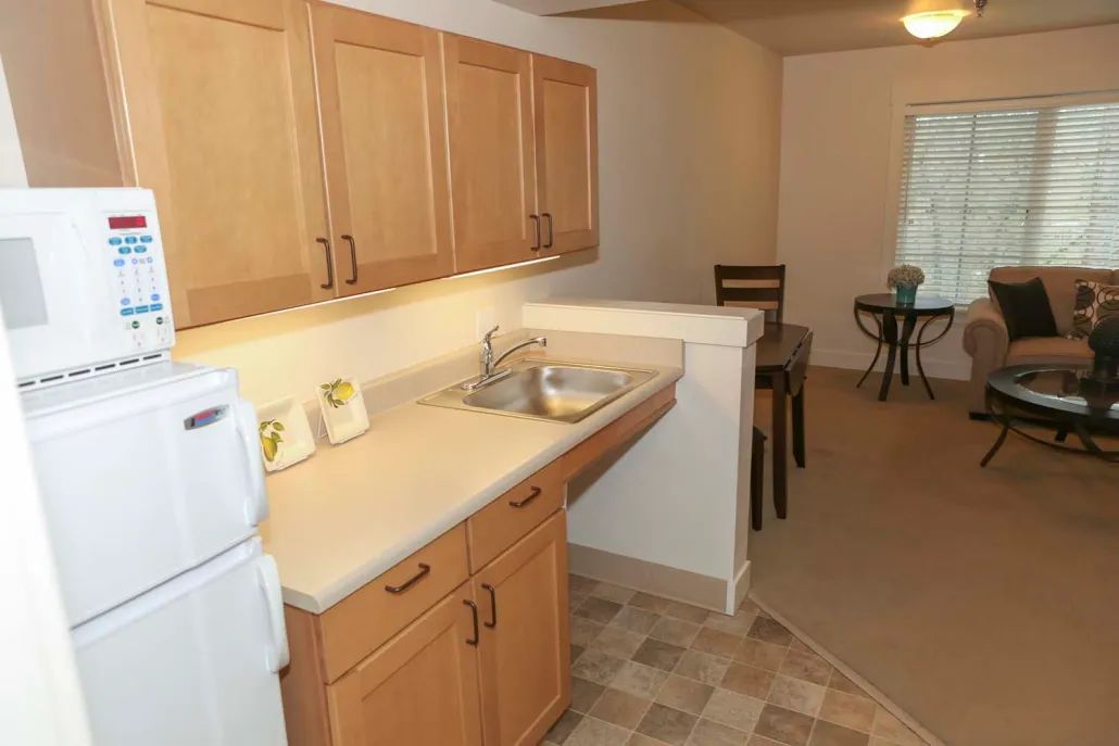 A compact kitchen with wooden cabinets and a small dining area in the background.