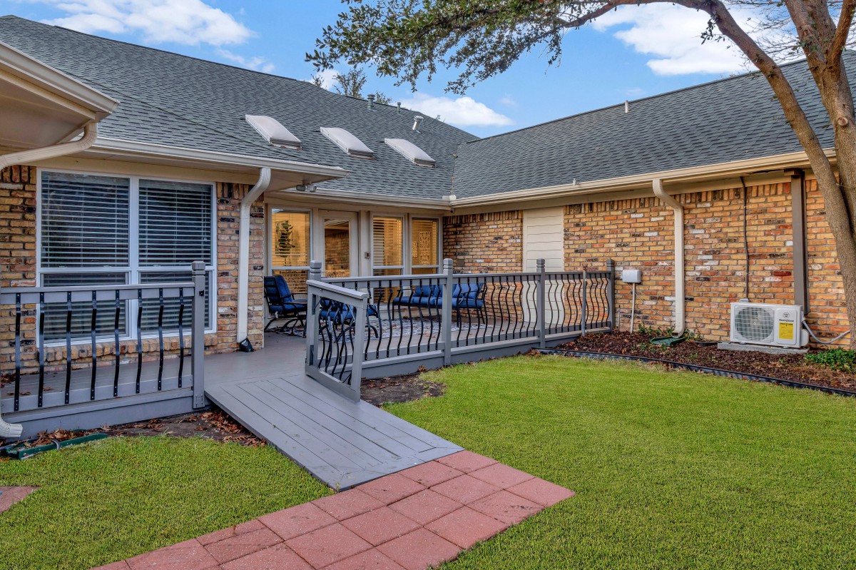 A charming brick house with a ramp leading to a cozy patio and well-maintained yard.