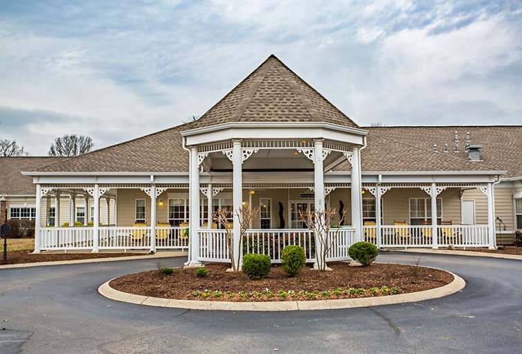 A building with a central gazebo structure at the entrance, surrounded by landscaped shrubbery.