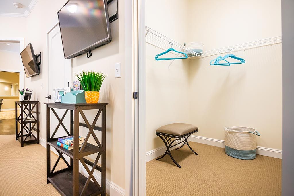 A neatly organized closet space with hangers and a bench next to a TV stand in a well-decorated room.