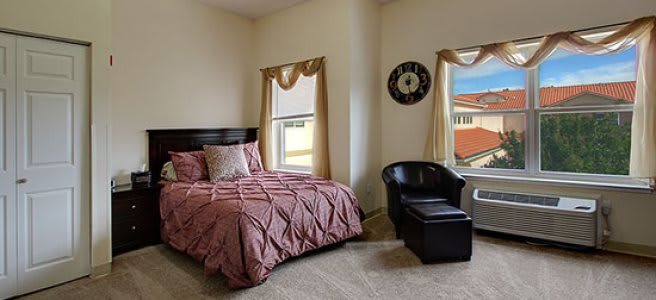 A cozy bedroom featuring a neatly made bed, a comfortable chair, and two windows with decorative curtains.