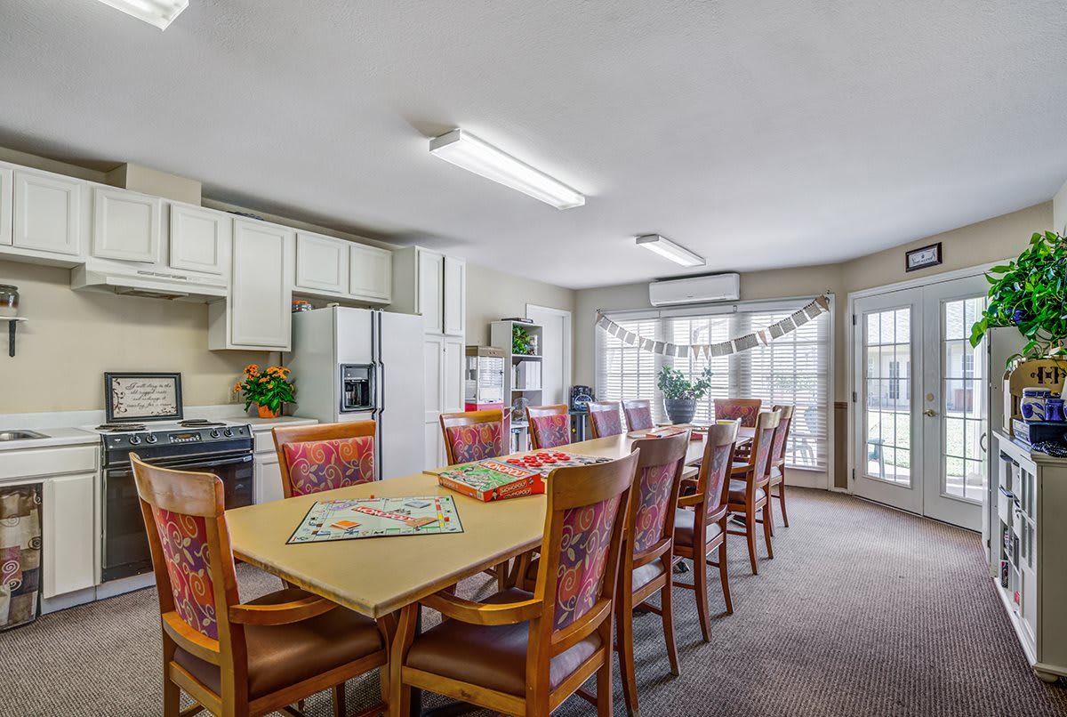 A spacious dining room and kitchen area featuring a long table with chairs, bright lighting, and large windows.
