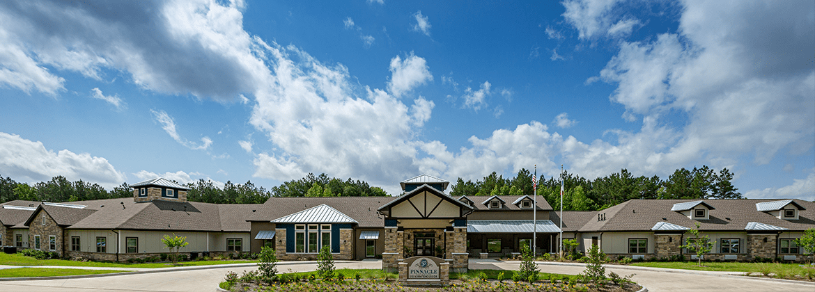 A modern building surrounded by greenery under a bright blue sky with clouds.