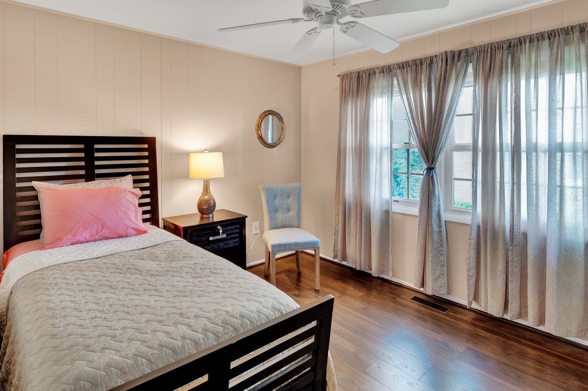 A cozy bedroom with a bed, bedside lamp, chair, and window with curtains.