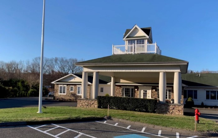 A building with a prominent covered entrance and columns in front of a parking lot under a clear blue sky.