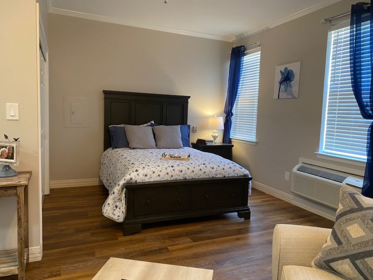 A cozy bedroom with a bed, pillows, and a bedside lamp, featuring wooden flooring and decorative elements.