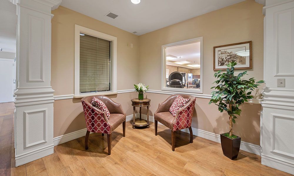 A cozy waiting area with two patterned chairs, a small table, and decorative plants.