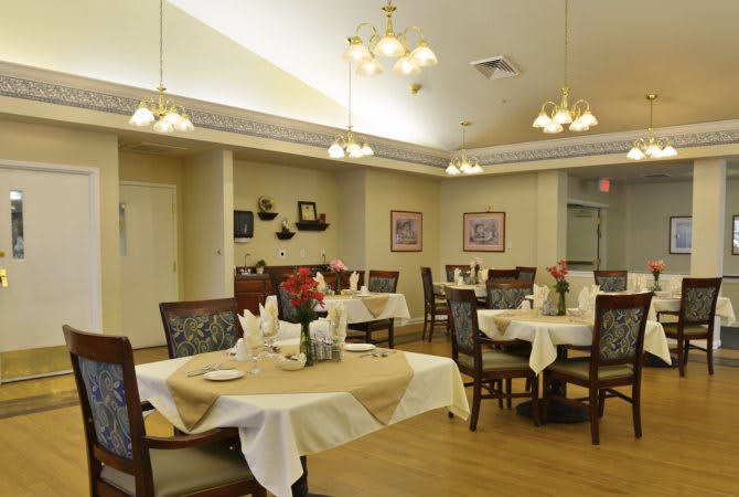 A well-decorated dining room with neatly arranged tables and chairs, featuring warm lighting.