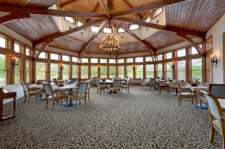 A spacious and elegant restaurant interior with a wooden ceiling and large windows.