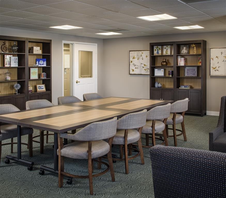 A well-organized conference room featuring a large meeting table and chairs, surrounded by shelves filled with books and decorative items.