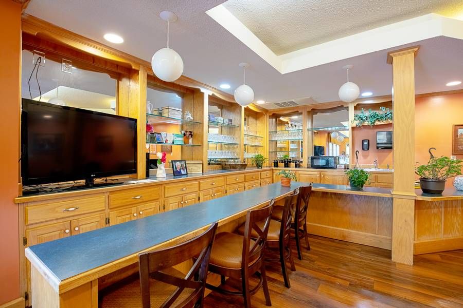 A modern office space with wooden desks, chairs, and shelving units, featuring a television and pendant lighting.