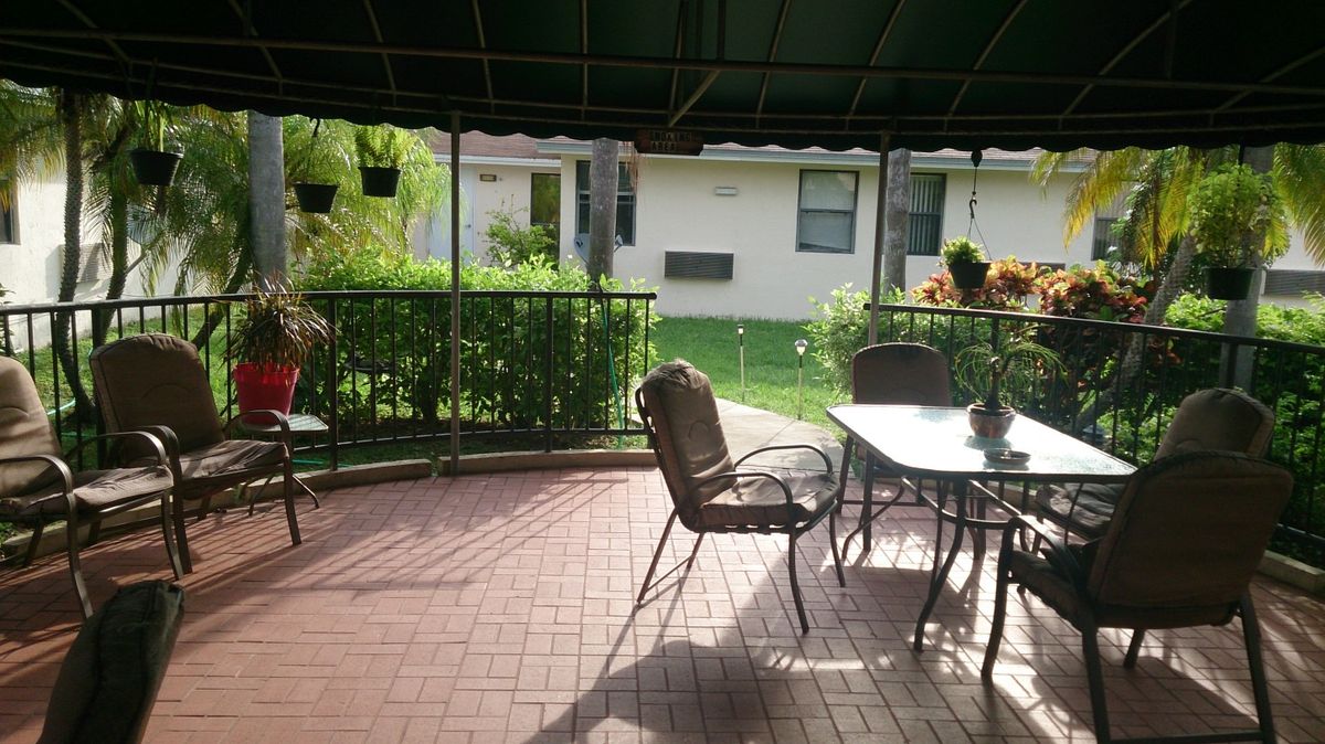 A cozy patio with a table and chairs under a canopy, overlooking a garden.