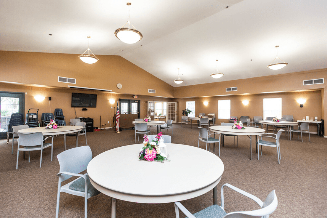 A spacious dining area with round tables and chairs, decorated with floral centerpieces.