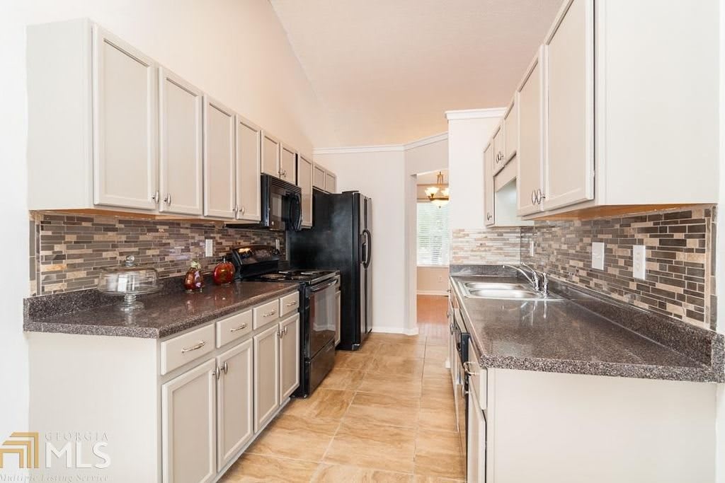 A modern kitchen with white cabinets, dark countertops, and stainless steel appliances.