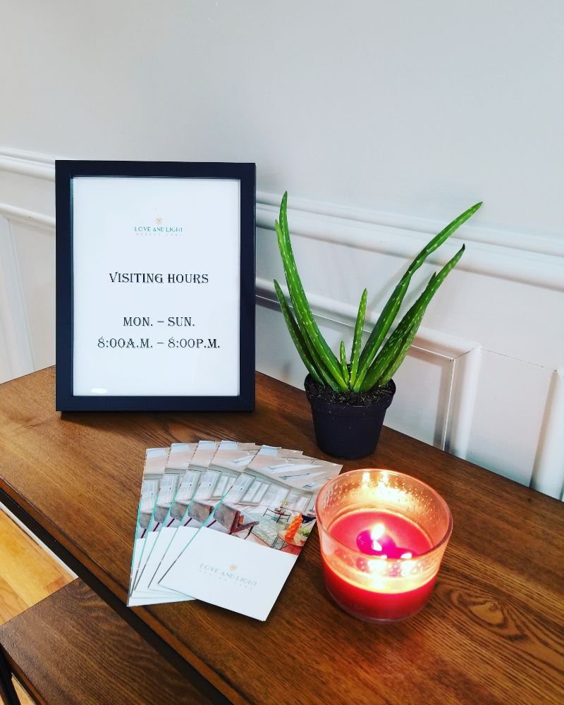 A welcoming setup features a framed sign, a small potted plant, a lit candle, and brochures arranged neatly on a table.