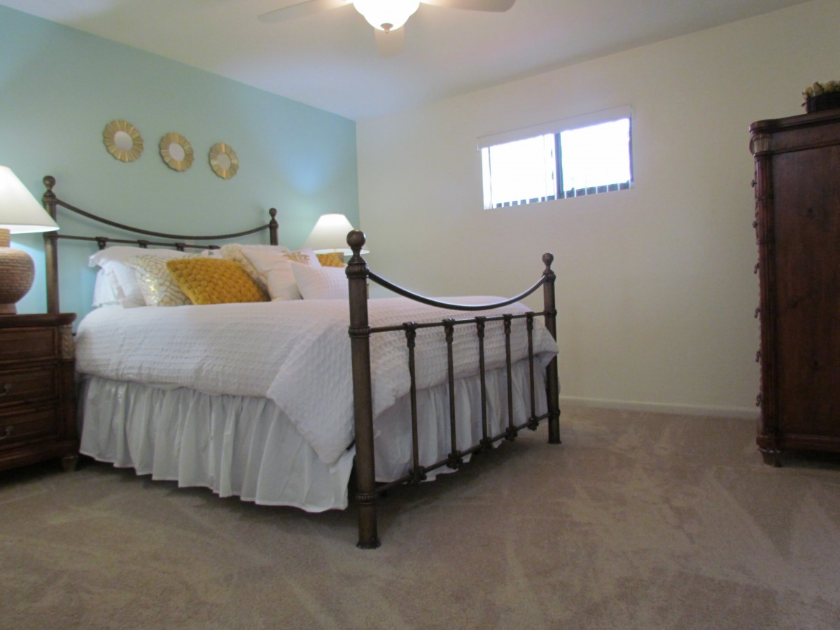 A cozy bedroom featuring a metal-framed bed with white bedding and yellow accent pillows, complemented by a soft carpet and warm lighting.