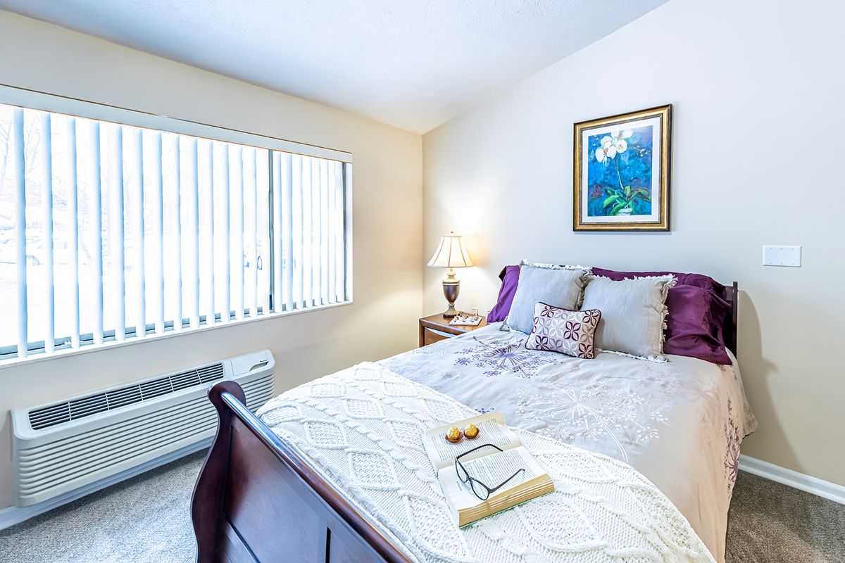 A cozy bedroom with a neatly made bed, a side table lamp, and a painting on the wall.