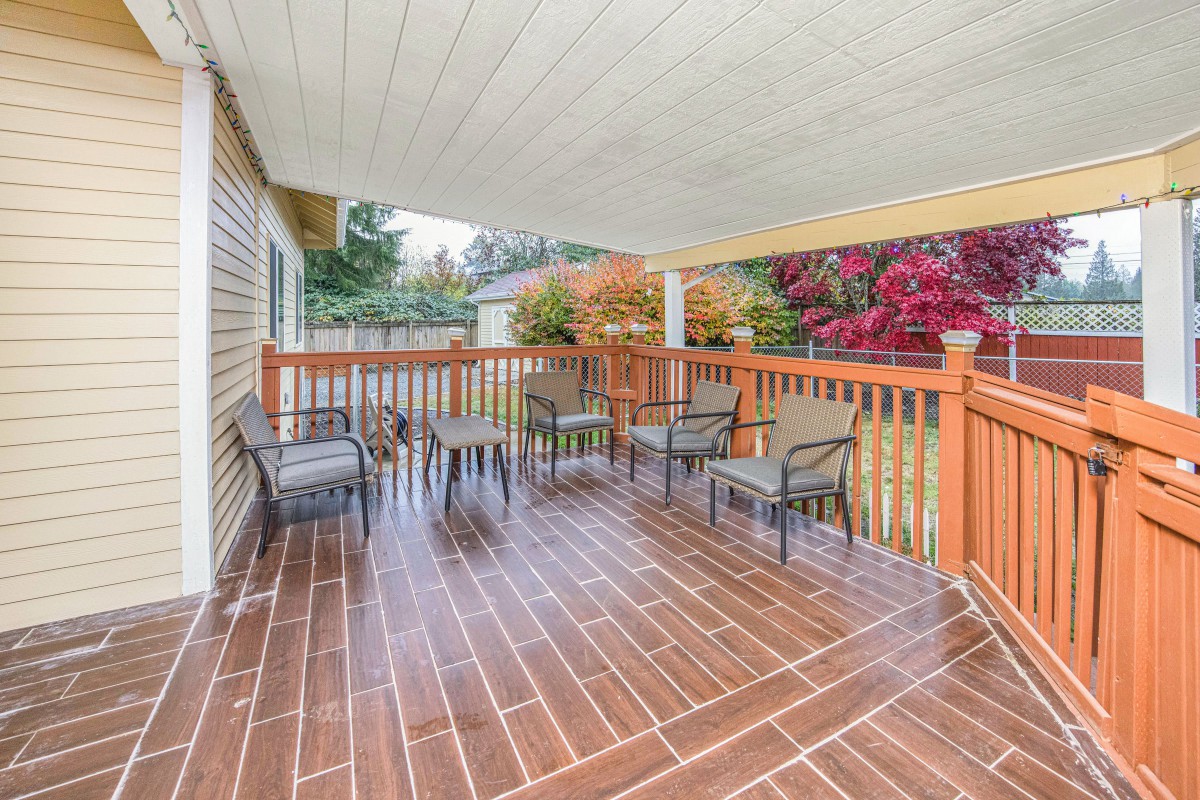 A covered wooden deck with outdoor seating and a table, surrounded by a backyard garden.