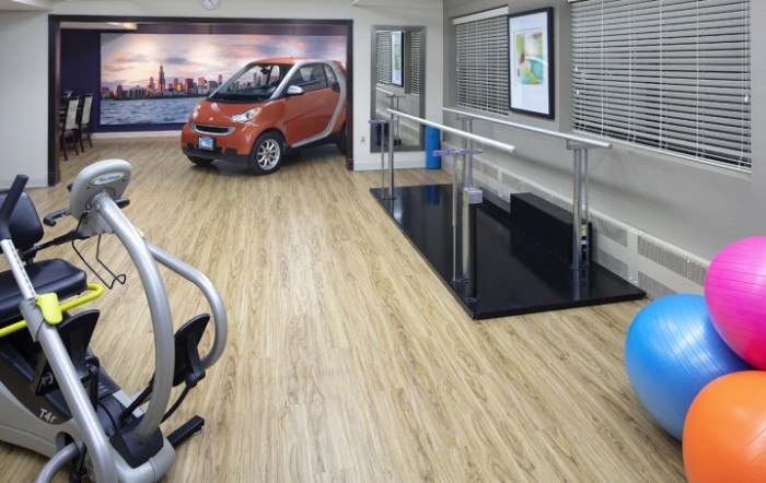 A modern rehabilitation center featuring a small car, exercise equipment, and wooden flooring.