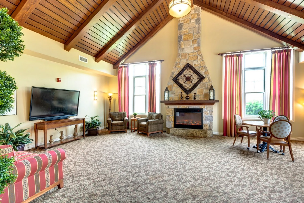 A spacious living room with high ceilings and a stone fireplace, featuring comfortable seating and large windows.