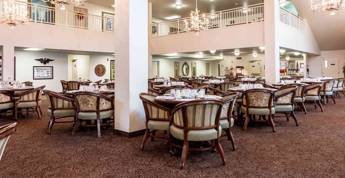 A spacious dining area with neatly arranged tables and chairs, featuring a chandelier and a carpeted floor.