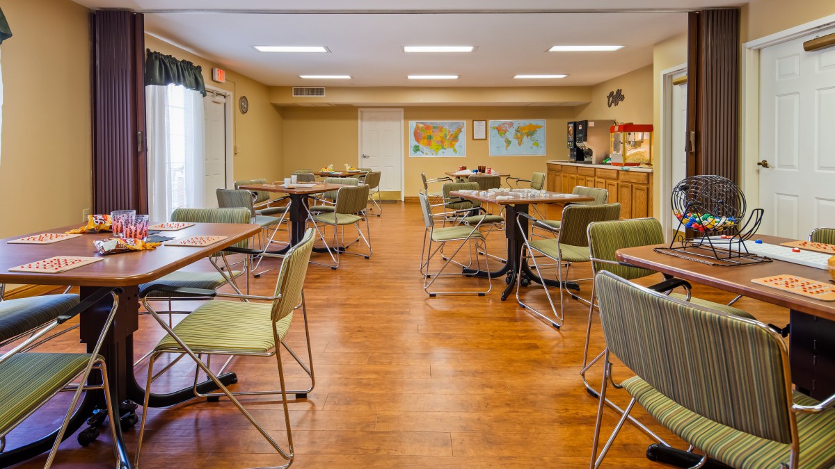 An educational space with tables and chairs, featuring a projector and world maps on the wall.