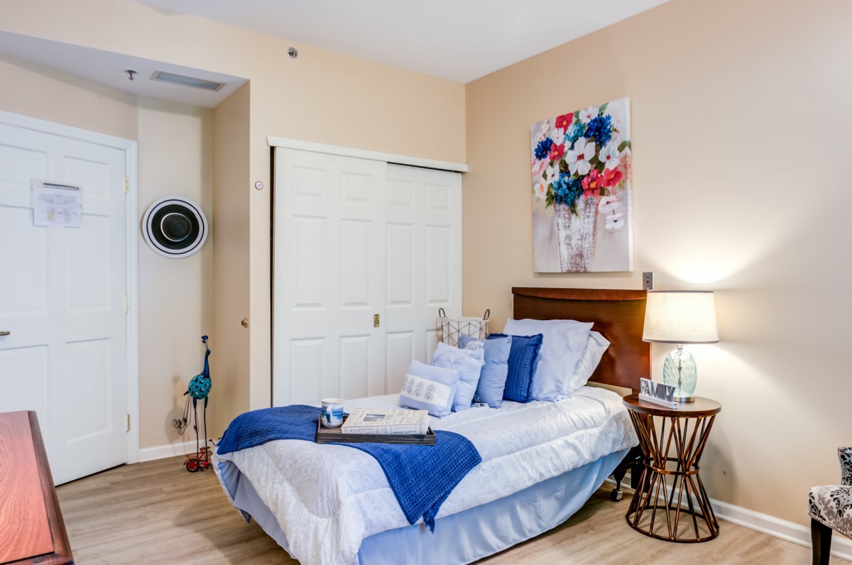 A cozy, modern bedroom with a neatly made bed, adorned with blue accents and a vibrant floral painting above the headboard.