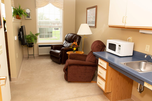A cozy living area featuring comfortable chairs, a small kitchen space with a microwave, and natural light filtering through the window.