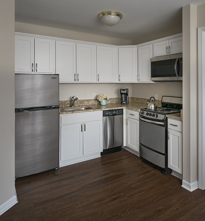 A modern kitchen with white cabinets, stainless steel appliances, and wood flooring.