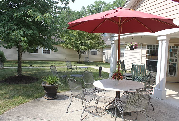 A cozy backyard patio with a table, chairs, and a red umbrella under the sun.